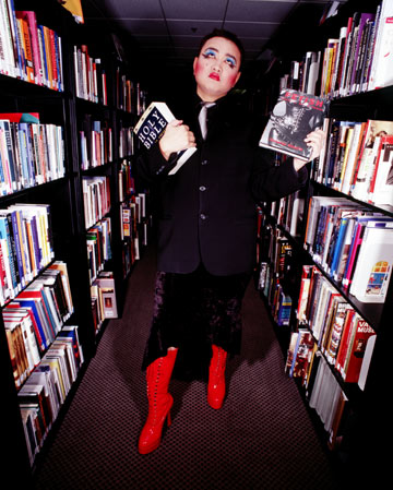 asian man dressed in drag in library holding two contradicting books